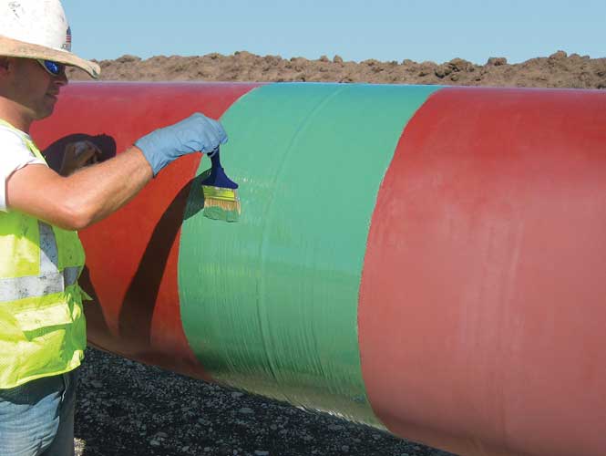 Worker applying a protective coating to an exposed pipeline